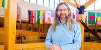 John Vucetich in the CFRES atrium with international flags hanging behind him.
