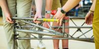 A close-up photo of steel bridge construction, with the words â€œMichigan Techâ€ visible along a steel beam among working hands.