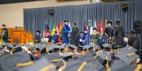 Students receiving diplomas on stage at 2024 Midyear Commencement, seen above the caps of those sitting down.