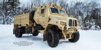 A large, tan-colored tactical vehicle stands parked outside in the snow.