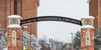 Archway with full univesity name in foreground with snow-covered trees and buildings in the background.
