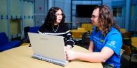 Two students talking and looking at a laptop, sitting in a round study lounge in Rekhi Hall.