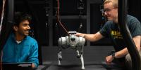 Two researchers test a quadruped robot walking on a treadmill in a lab setting.