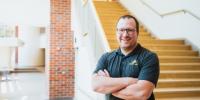Zack Fredin stands with arms crossed in front of open staircase.