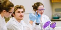 Ben Amat holds up a petri dish while sitting in the lab with two other students.