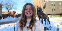Kallee McCone in a Michigan Tech sweatshirt in front of the Husky Statue during a sunny winter day.