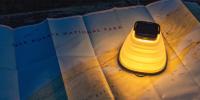 A small artificial lamp sheds dramatic yellow light on a paper map of Isle Royale National Park unfurled on a table.