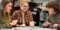 Sarah Hoy, Tara Bal and Grace Moeggenborg sit around a table covered in more than 50 small vials, each containing a winter tick used in their research.