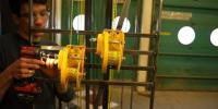 Danny Ezzo uses a cordless drill to operate yellow pulley systems attached to metal bars indoors.