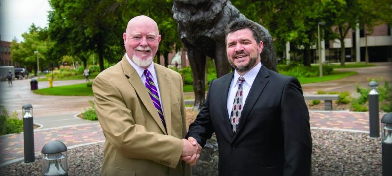 Gene Klippel and Dean Johnson shaking hands in front of the Husky statue