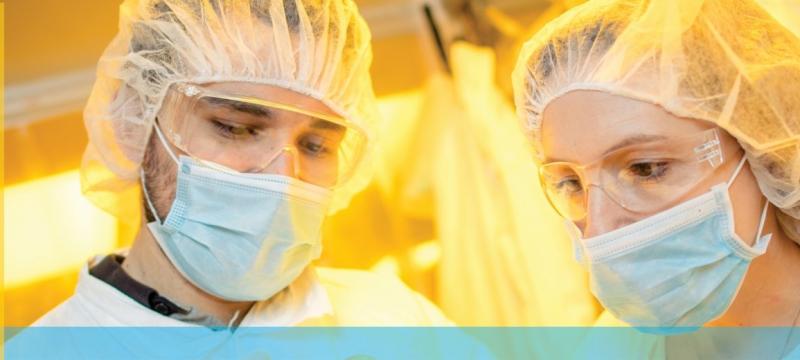 Two people with hair nets, masks, and safety glasses.