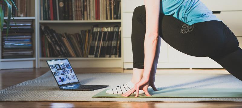 A person doing a yoga pose while watching a video on a laptop.
