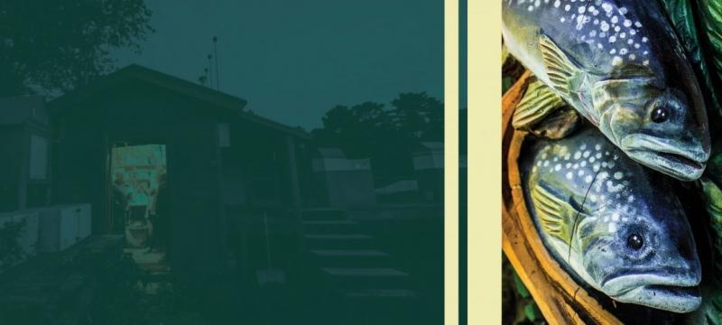A faded image of a hut at dusk next to brightly painted fish and leaves carved on a pole.