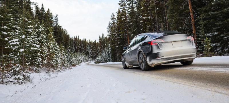 The back of a snowy car driving on a snow covered road through a forest.