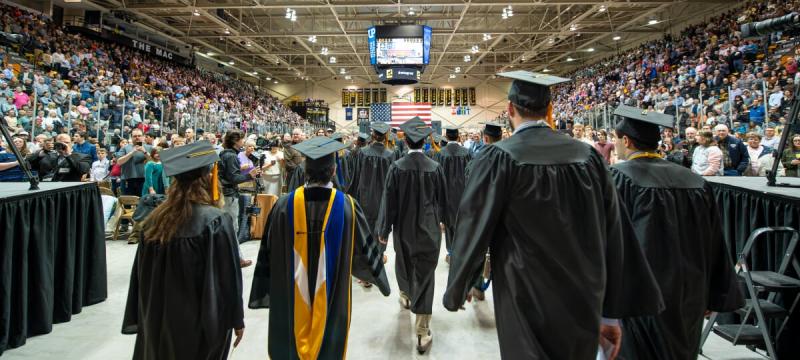 Students in caps and gowns walking into the commencement ceremony in the ice arena.