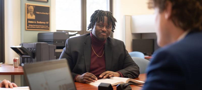 Elijah Joseph sitting at a table with a book. Other people are visible to the sides.