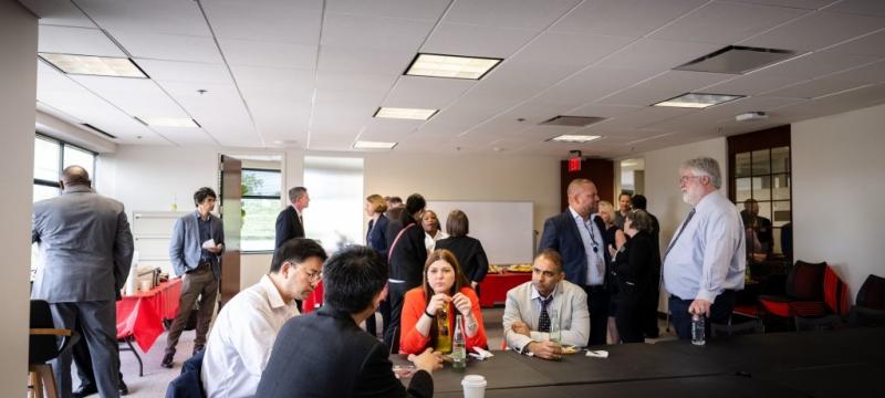 Researchers from two universities sit at a table and gather in groups around a room where food is set out, getting to know each other and envisioning collaborations.