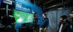 Students gathered around a professor pointing at a large screen with the russells technical products logo above it.