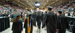 Students in caps and gowns walking into the commencement ceremony in the ice arena.