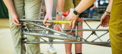 A close-up photo of steel bridge construction, with the words “Michigan Tech” visible along a steel beam among working hands.