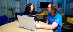 Two students talking and looking at a laptop, sitting in a round study lounge in Rekhi Hall.