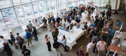 Large group of people attending an academic poster presentation in a spacious, sunlit hall with floor-to-ceiling windows.