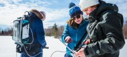 Three Michigan Tech researchers collect data on a snowy field site using a laptop computer and backpack spectrometer.