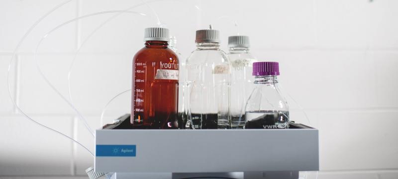 Four bottles of different shapes and sizes that all have liquid measurement marks on their sides sit in a tray.