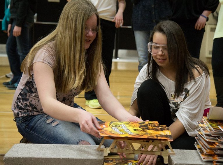 Two students test the strength of their popsicle stick bridge.