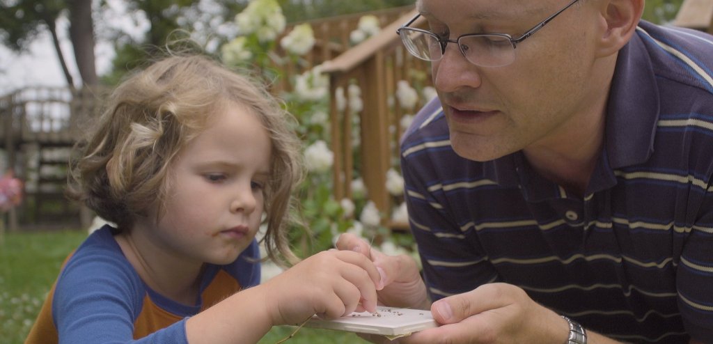 Thomas Werner and his daughter look at fruit flies outside the compost tumbler at their house in Houghton, Michigan.