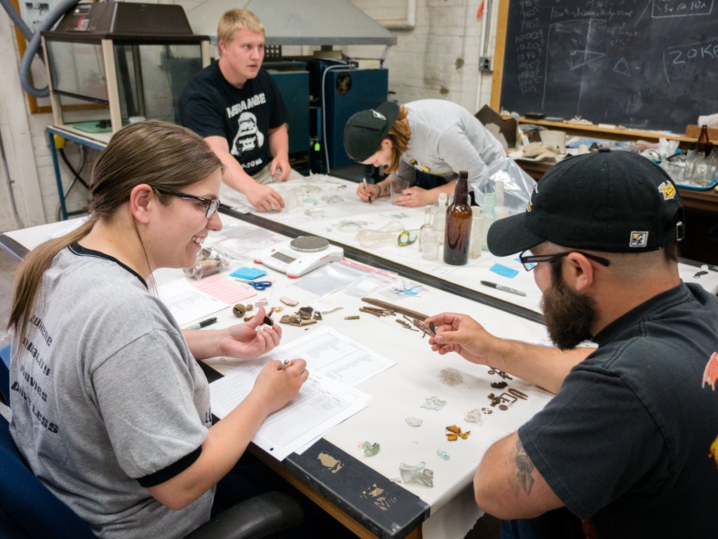 Morgan Davis, Joe Iwaniki, Savannah De Luca, and James Schwaderer sort and catalogue artifacts from the excavation in the archaeology lab in the Academic Offices Building Annex. Image Credit: Kelley Christensen