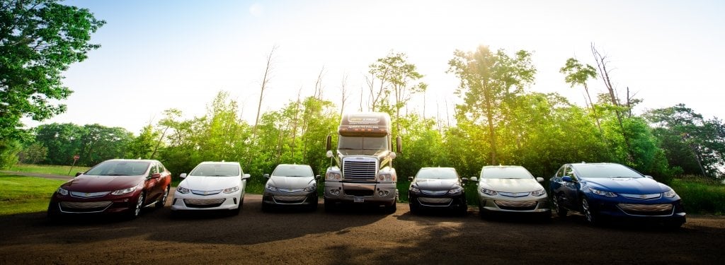 cars in a semicircle with a semi-truck in the middle and trees in the background