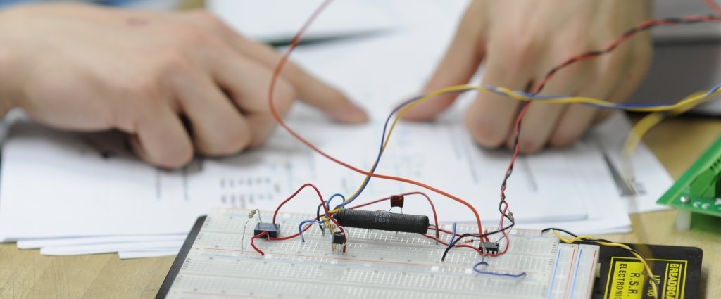   The hands of a student working in the Michigan Tech school of technology lab on an electronic chip and electroincis board with wiring and schematics.  