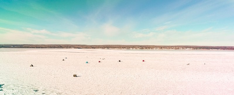 ice fishing huts on white ice under a blue sky with clouds