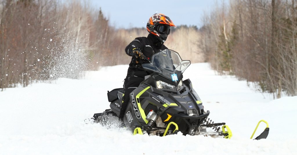 A snowmobile rider wearing an orange helmet rides a black and bright yellow snowmobile. 