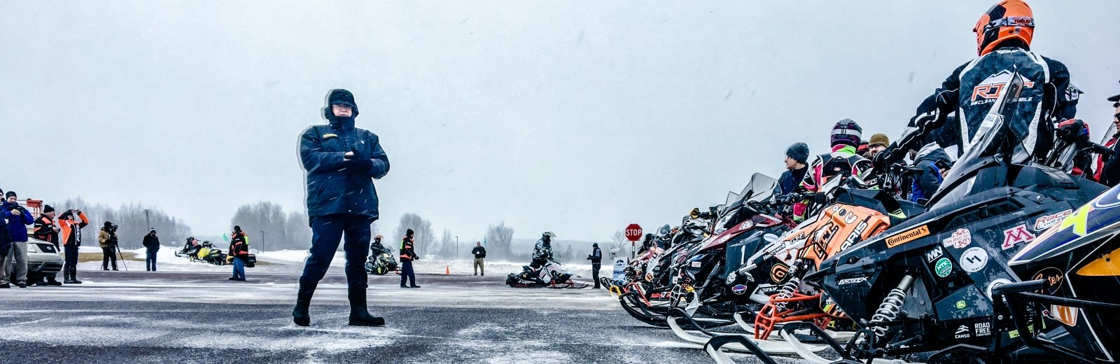 A man standing next to the lineup of snowmobiles and their riders.