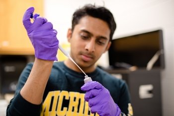A lab tech wearing purple gloves uses a pipette to extract serum