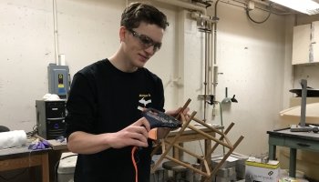 a young man with a glue gun in a basement work area glues sticks together to make a bunkbed