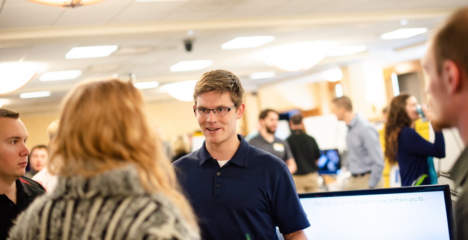 A male student talks to a woman. Two students look on. 