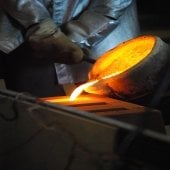 A hand pours liquid metal into a mold