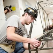 A young man works on fastening parts of a steel bridge he is wearing a black hard hat and concentrating