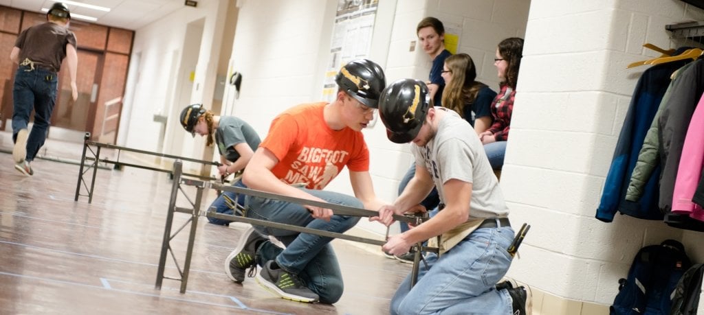 Seven young people in a hall with pieces of a steel bridge near a coat closet. 