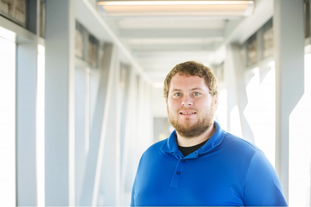 A bearded young man stands in a sun-basked corridor 