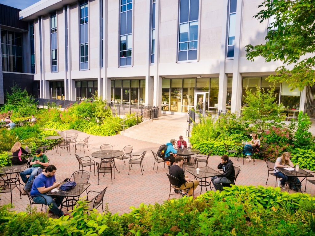 Campus mall with students sitting at tables outside library