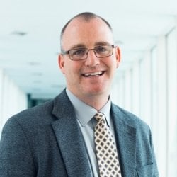 White male wearing glasses smiles at camera.