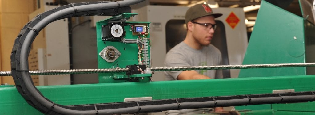 A student stands between a green machine.