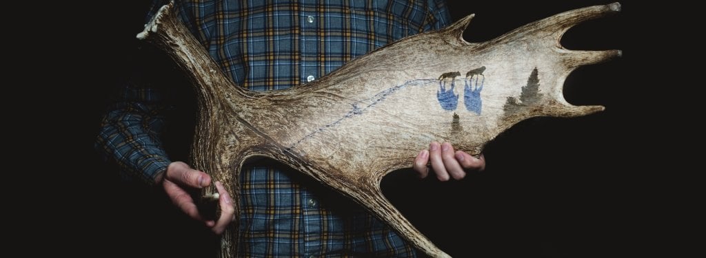 A man in blue flannel holds a moose antler. 