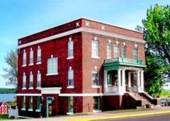 the exterior of a vintage brick building housing Houghton County Historical Society museum witha green lawn and a tree 