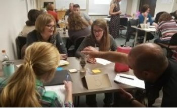 four teachers sitting at a table doing an experiment with a plain plastic bucket