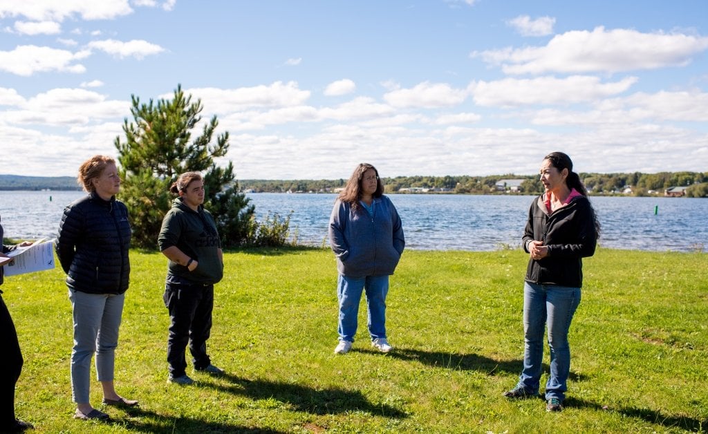 Four people stand in a semi-circle on grass in front of Lake Superior